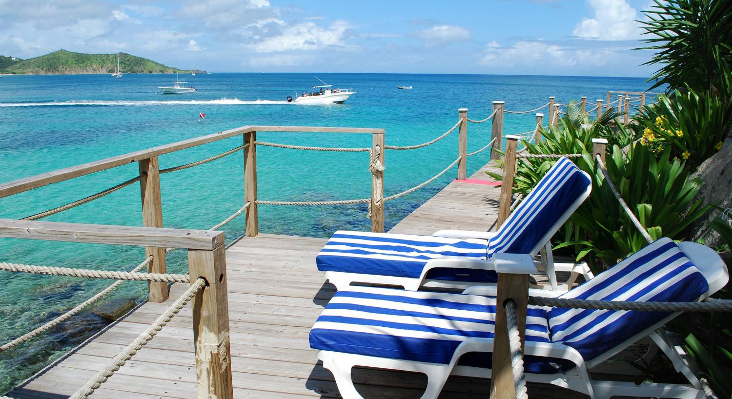 Two beach chairs on a deck overlooking crystal clear water. 