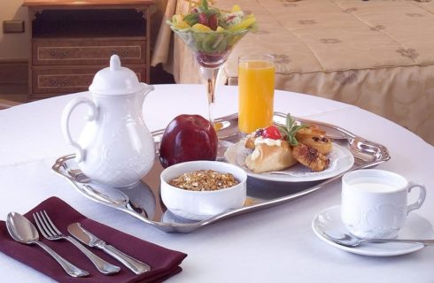 Breakfast tray with beverages, cereal and fruit on a white table